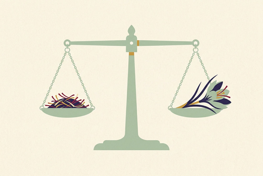 A small balance scale holding a measured pinch of saffron threads on one pan and a saffron crocus flower on the other