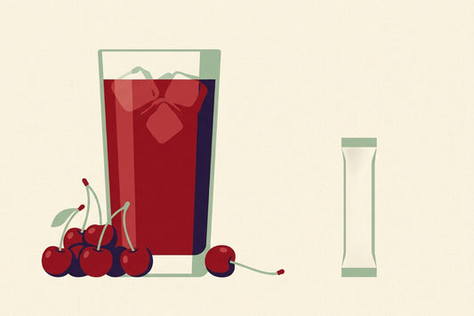 A tall glass of deep red tart cherry juice with a cluster of cherries beside it, and alone across the frame a single small plain unbranded stick sachet