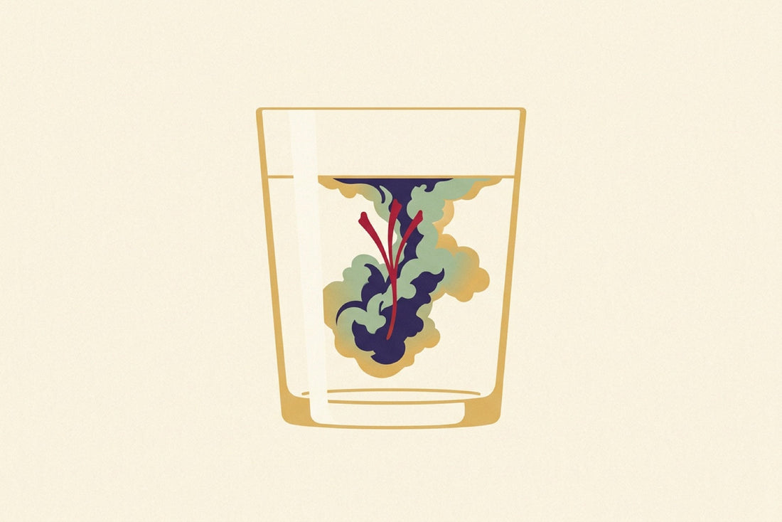 A single crimson saffron stigma in a glass of water, its red pigment blooming outward through the water