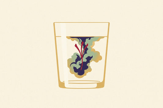 A single crimson saffron stigma in a glass of water, its red pigment blooming outward through the water