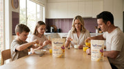 A family of four at the breakfast table, the kids with Bright AM sachets and their mum with a Rise AM sachet, the pouches on the table