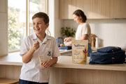 A boy in school uniform at the kitchen bench with a Bright AM sachet and a spoon of honey before school