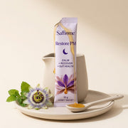 A Restore PM sachet torn open, honey running onto a spoon, a passionflower and lemon balm beside it