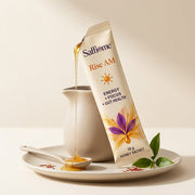 A Rise AM sachet torn open, honey running onto a spoon, green tea leaves and saffron threads beside it