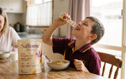A boy squeezing a Bright AM honey sachet straight into his mouth at the breakfast table, the pouch beside his cereal