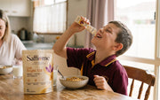 A boy squeezing a Bright AM honey sachet straight into his mouth at the breakfast table, the pouch beside his cereal